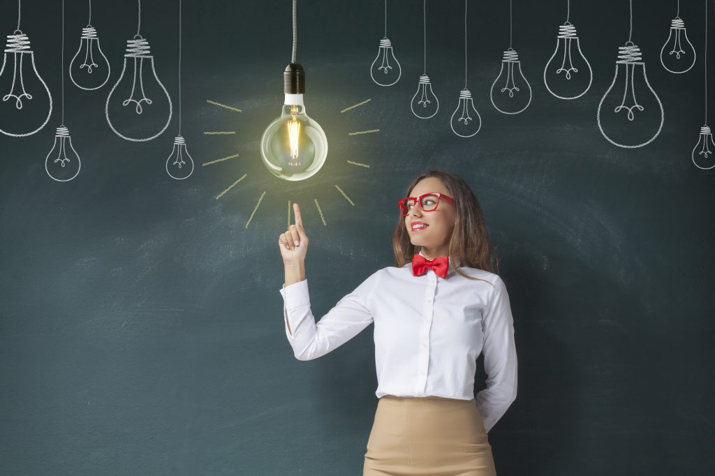 Young teacher pointing light bulb on blackboard background